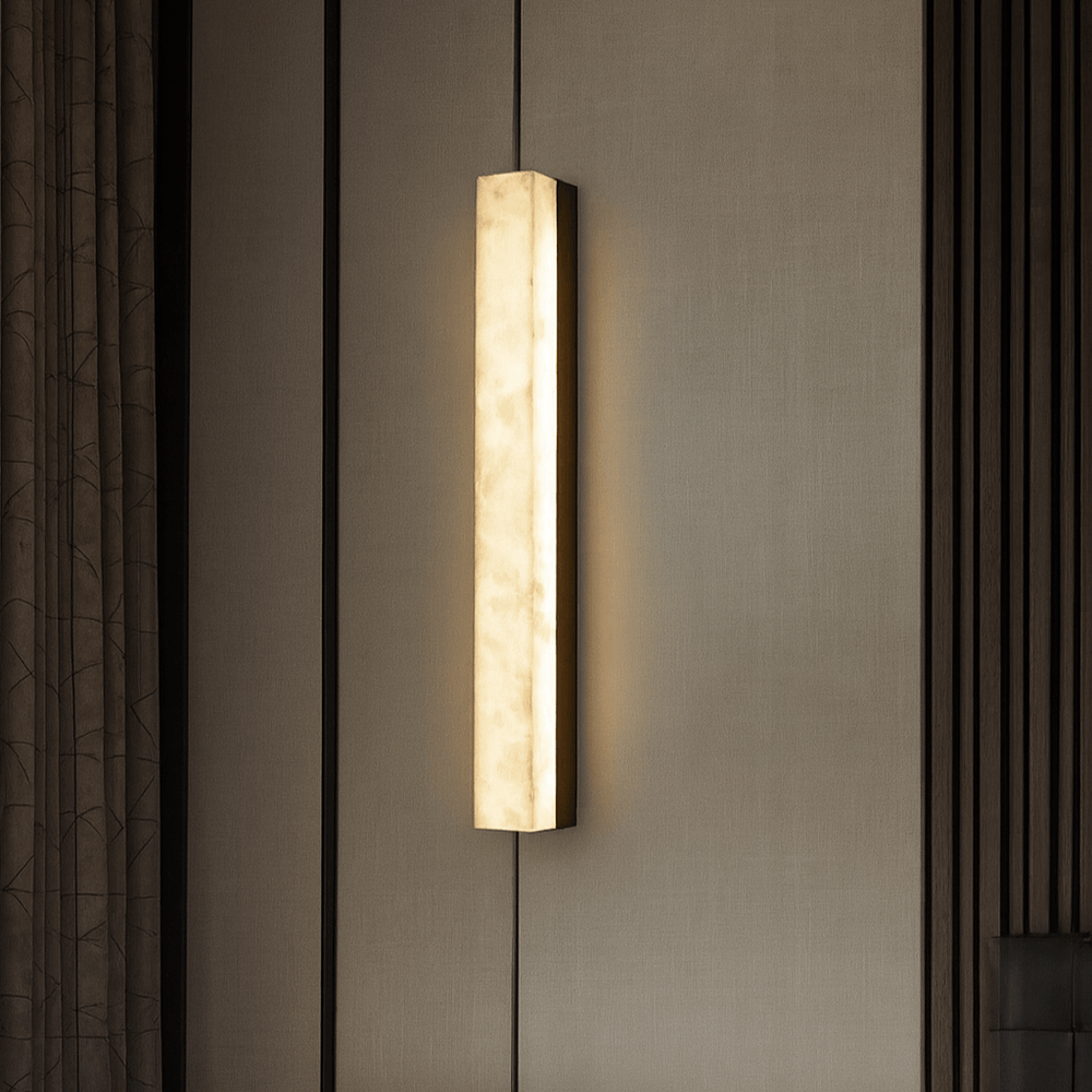 
                  
                    The Linden Marble Sconce, Black by Morsale.com casts a warm, soft glow on a beige textured wall with vertical dark trim on the right and patterned curtains to the left.
                  
                