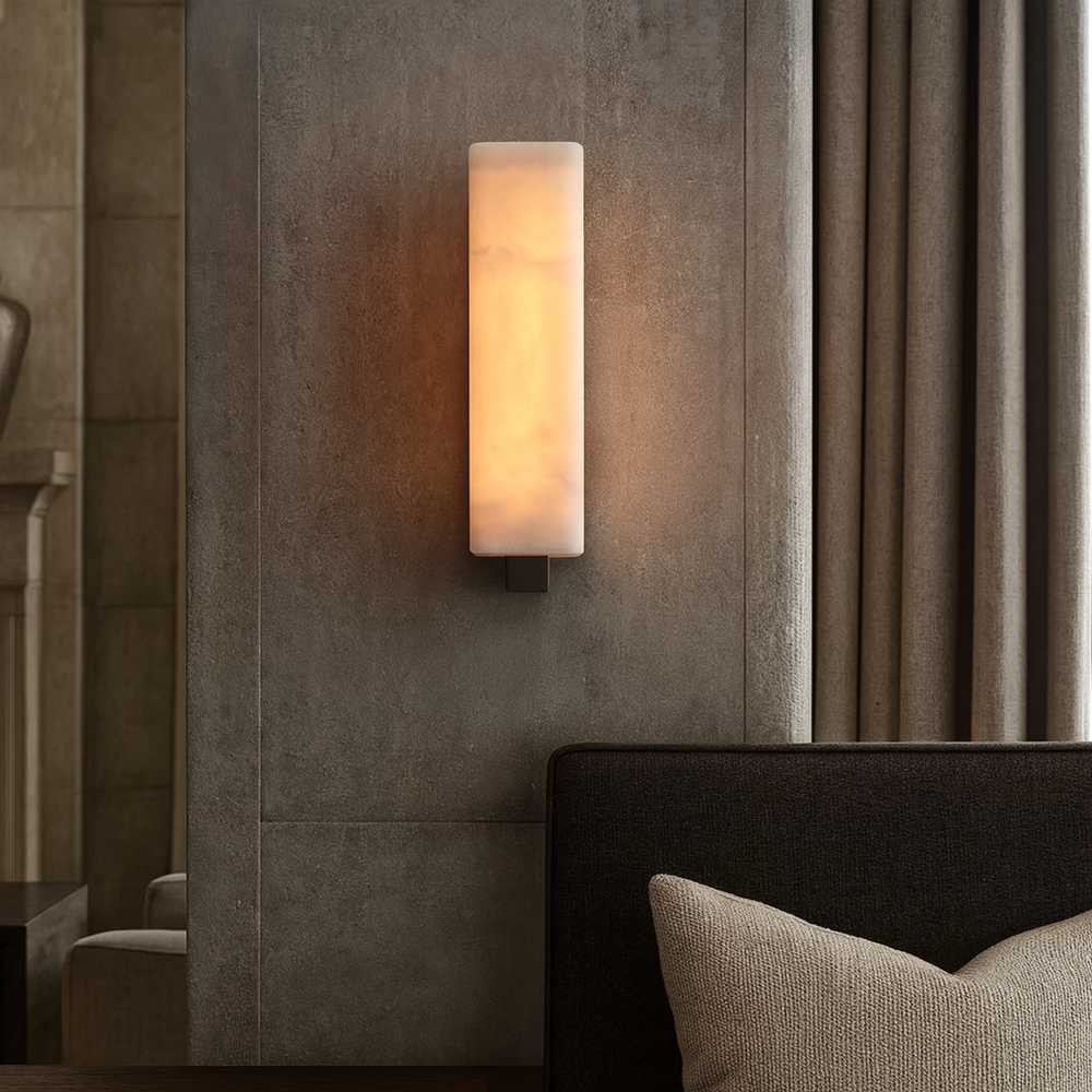 The Alton Marble Wall Lamp by Morsale casts a warm glow on a textured gray wall beside beige curtains and a dark sofa, adding modern style to the minimal living space.