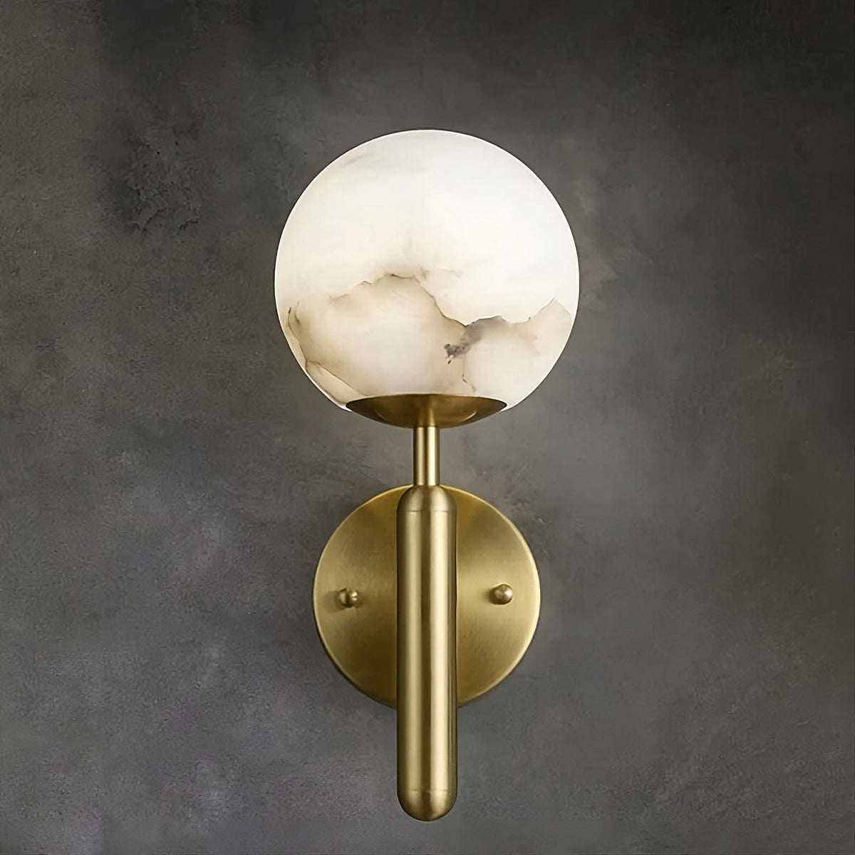 A wall-mounted brass light source featuring a cylindrical base and a spherical, translucent white glass shade with marble-like veining. The background is a smooth, dark gray surface, highlighting the warm, elegant design of the dimmable Natural Marble Sphere Wall Sconce by Morsale.com.