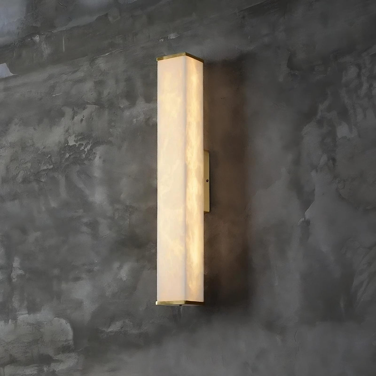 A modern, vertically oriented Natural Marble Indoor Wall Sconce Light by Morsale.com with a rectangular design emits a soft, warm light. The sconce is mounted on a textured, dark gray concrete wall, providing a sleek and contemporary aesthetic.