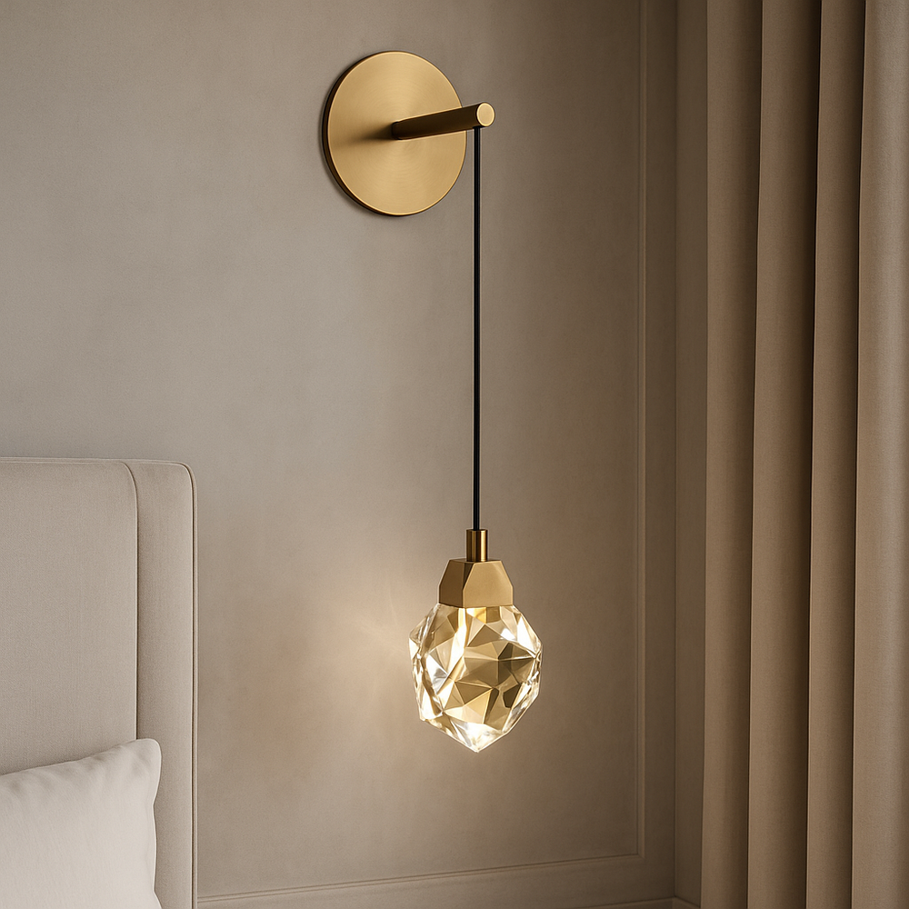 The Bari Crystal Wall Sconce by Morsale.com, featuring a brushed brass finish and faceted glass pendant, adds a warm ambient glow beside a beige upholstered bed and neutral curtains.