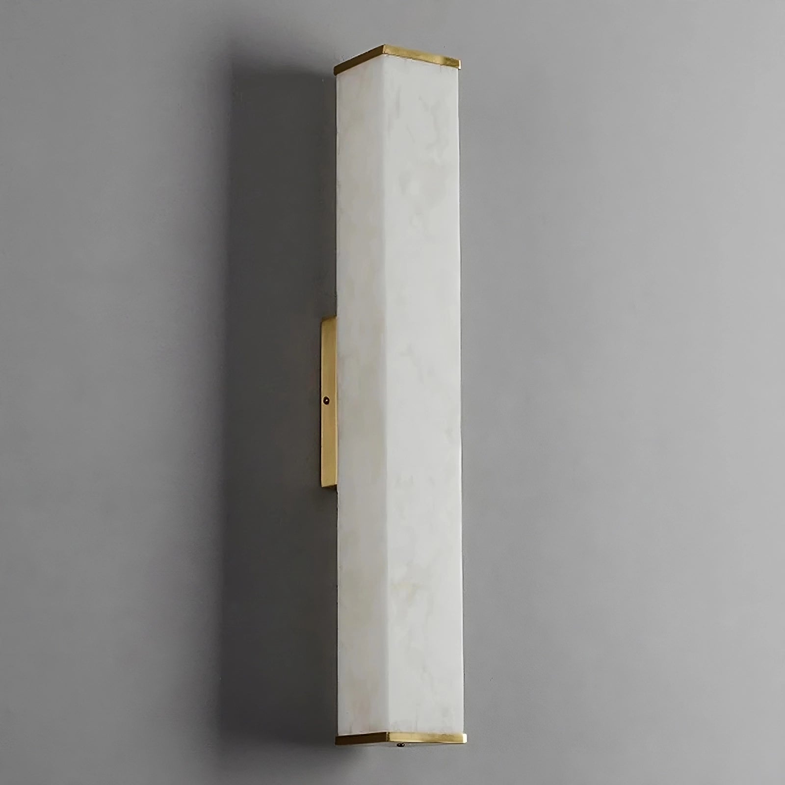 A sleek brass light fixture with a vertical rectangular design features a white frosted glass shade and brass accents at the top and bottom. The Natural Marble Indoor Wall Sconce Light by Morsale.com is mounted on a gray wall, adding to the minimalistic, modern style.