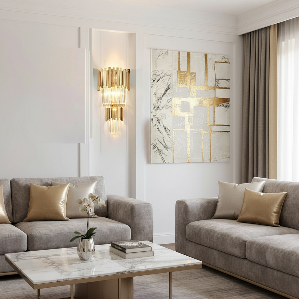 
                  
                    A modern living room with two gray sofas, gold and beige pillows, a marble coffee table with a potted orchid, abstract gold and white wall art, luxury lighting by Morsale.com's Gio 23" Crystal Wall Sconce, and floor-length beige curtains.
                  
                