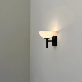 The Morsale Spanish Marble & Copper Antique Sconce, featuring a black mounting fixture and a white, semi-circular shade, casts a soft, warm glow that gently highlights a minimalist white wall while incorporating an elegant hint of copper antique sophistication.