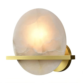 A modern wall sconce featuring a circular, frosted glass shade that emits a warm, soft light. The glass is mounted on a sleek, horizontal brass bar attached to a round brass backplate. The minimalist design combines contemporary style with an LED light source and elegant materials. Introducing the Natural Marble Wall Light Sconce by Morsale.com.