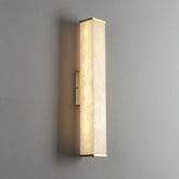 A vertical, rectangular wall sconce with a frosted, diffused glass cover emits a soft, warm light. The Morsale.com Natural Marble Indoor Wall Sconce Light, mounted on a gray wall and featuring metal accents at the top and bottom in a gold finish, boasts an LED light source for energy efficiency.