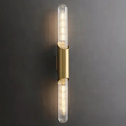 A modern wall sconce with a vertical, cylindrical design features two elongated, clear glass bulbs on either end. The bulbs are encased in a sleek brass holder, emitting warm light against a dark gray background, exemplifying elegant lighting with the Palermo 23" Brass Wall Sconce Light by Morsale.