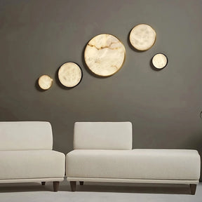 A contemporary living room includes two white sofas on a light gray floor. On the dark gray wall, five circular illuminated decorations are arranged in a diagonal pattern, similar to the elegant design of the Moonshade Marble & Copper Ceiling Light by Morsale. A small round black table with a subtle marble finish is positioned to the left of the sofas.