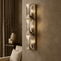 Brookhill 3-Light Crystal Wall Sconce with three stacked crystal glass prisms on an iron frame, glowing warmly on a taupe wall.