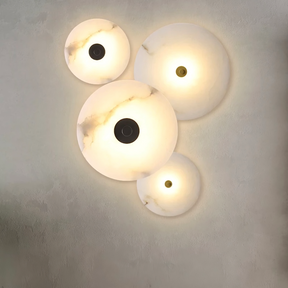 The Moonshade Natural Marble Wall Sconce set by Morsale.com includes four circular lights of varying sizes, emitting a warm glow. Their elegant marble design on a textured wall adds a modern and artistic ambiance.