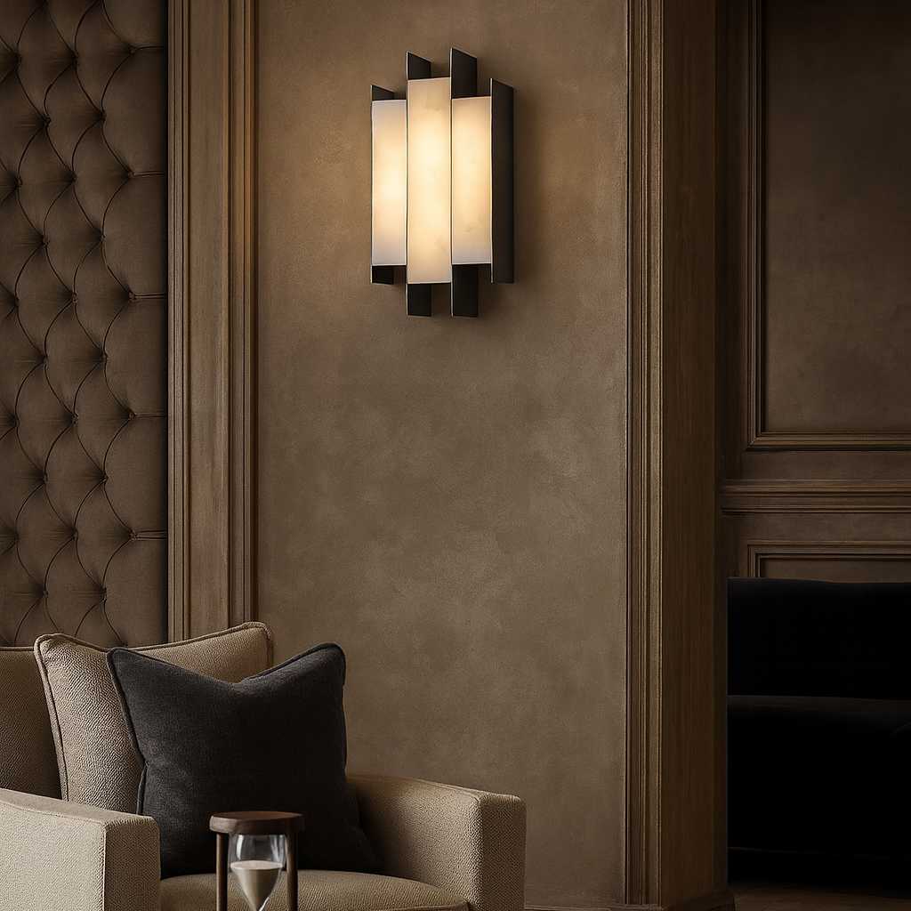 The Arden Marble Sconce by Morsale, featuring layered rectangular panels and soft lighting, is mounted on a beige wall above a plush armchair with dark pillows in an elegant, neutral-toned living room.