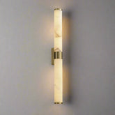 The 27" Moonshade Natural Marble & Copper Wall Sconce by Morsale features a contemporary design with two cylindrical natural marble shades arranged vertically on a copper fixture against a gray wall. It emits a gentle illumination from both ends, creating a soft, ambient glow.