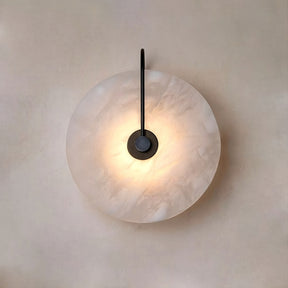 Introducing the **Moonshade Natural Marble Sconce Light** by **Morsale.com**: This circular wall sconce is expertly crafted from high-quality marble and features a marbled white shade that emits a gentle luminance. When mounted on a light-colored wall, its dark rod extends sleekly from the center, enhancing its minimalist and sophisticated aesthetic.