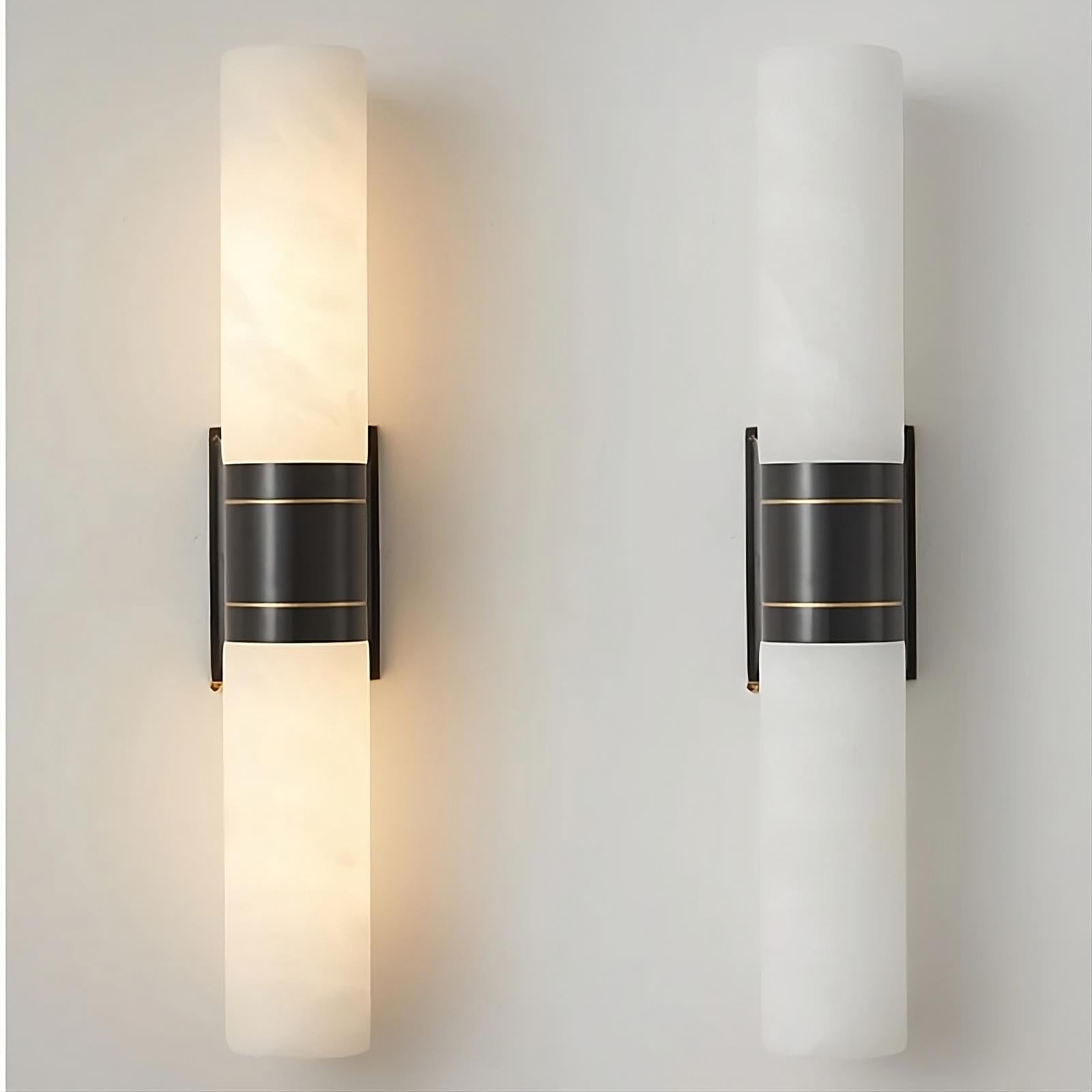 A pair of Natural Marble Indoor Wall Sconce Lights by Morsale.com with cylindrical white glass shades are shown. Both sconces, featuring a central black metal bracket and unique texture, add elegance to the plain, light-colored wall. The left sconce is illuminated, emitting a warm light, while the right sconce remains turned off.