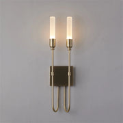 The Candela Contemporary Wall Sconce by Morsale showcases two vertical cylindrical lights on sleek brass stems, mounted on a rectangular base. This modern fixture enhances the gray wall with sophistication, fitting seamlessly into any interior design.
