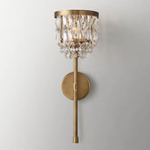 The Luxe Crystal Brass Wall Sconce by Morsale.com features a circular base and vertical rod adorned with hanging crystal prisms that catch light beautifully. These crystals are arranged in concentric rows, creating an elegant, cascading effect. This luxurious home decor item is perfectly showcased on a plain, light-colored wall.