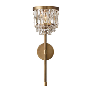 The Luxe Crystal Brass Wall Sconce from Morsale.com features a circular base and a slim, vertical rod. The light is beautifully encased in a shade adorned with hanging teardrop-shaped crystal prisms, making it an elegant and luxurious lighting fixture perfect for any sophisticated home decor setting.