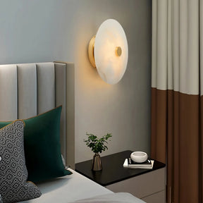 The modern bedroom showcases a Morsale Witney Copper & Marble Wall Sconce above the nightstand. A beige upholstered headboard pairs with green and black pillows, while the sleek copper design enhances the decor. Beige and brown curtain panels and a potted plant complete the stylish look.