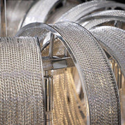 Close-up view of intricately designed, overlapping metallic rings with a grid-like texture that appear to be part of the Cadena Chain Tassel Modern Chandelier by Morsale.com. The rings reflect light, creating a shimmering and luxurious effect, and the adjustable ceiling wire length ensures perfect placement.