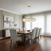 A modern dining room with a wooden table, eight beige upholstered chairs, sheer curtains, a sideboard, abstract wall art on paneled walls, and the Alleri Crystal Chandelier by Morsale.com as the statement lighting.