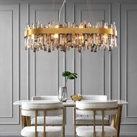 A modern dining room features a glass table, four upholstered chairs, a gold decorative bowl, a vase with green leaves, and the Morsale.com Asti Flush Mount as striking lighting against a gray paneled wall.