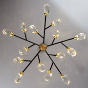 The Diamante Crystal Branch Chandelier, Black by Morsale.com features a central gold hub with black arms extending outward, each ending in gold and crystal cubes that form a starburst pattern. It casts a warm, elegant glow against a neutral ceiling with its LED bulbs.