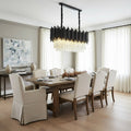 The Vigo Crystal Dining Room Chandelier by Morsale.com, with a modern design of glass and black metal rods, hangs over a candlelit table in a bright dining room with white paneled walls and artwork.