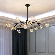 The Diamante Crystal Ceiling Light Fixture by Morsale.com hangs from the ceiling, featuring modern geometric glass shades and black branches with multiple arms extending outwards. Each arm holds a cube-like light fixture. The room showcases white and dark curtains against a light blue wall.
